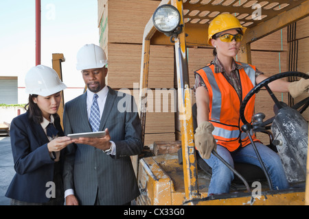Engineers using tablet PC with female industrial worker driving forklift truck Stock Photo