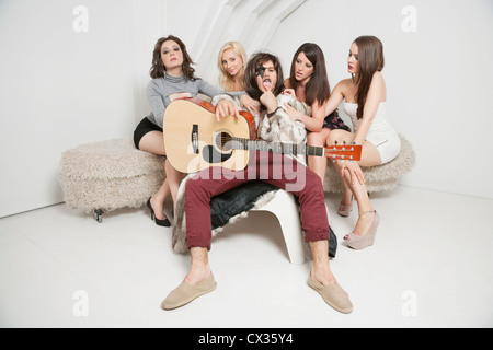 Portrait of young male guitarist sitting amid young female friends Stock Photo