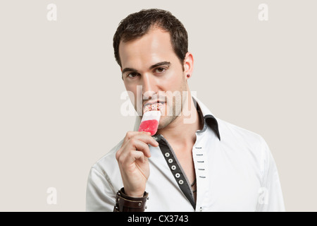 Portrait of young man eating ice cream candy against gray background Stock Photo
