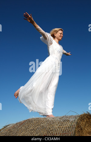 Young woman standing on a straw bale against a blue sky Stock Photo