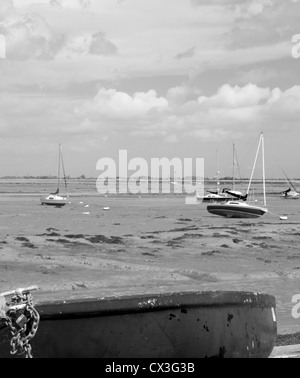 Mono of row boat with a background of boats on a low tide in Langstone Harbour. Stock Photo