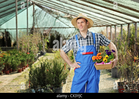 Young worker holding a basket full of flower pots and posing in a garden Stock Photo