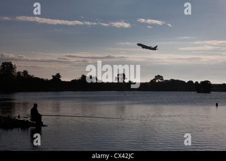 Man fishing in Yeadon Tarn as an aircraft takes off from Leeds Bradford Airport. Stock Photo