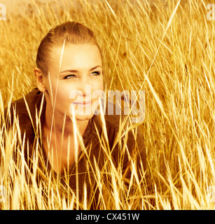 Picture of pretty woman sitting on wheat field, closeup portrait of cute young lady on golden ryes background, autumn harvest Stock Photo