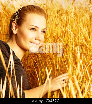 Photo of attractive smiling girl sitting in golden wheat field, closeup portrait of beautiful young blond female Stock Photo