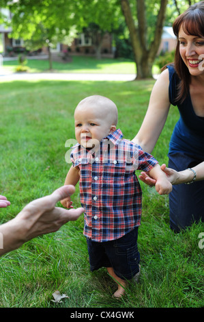 White Caucasian Mother Father with baby son taking his first steps learning to walk outdoors Stock Photo