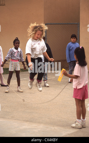 A blonde middle school girl happily skips rope with her multiethnic classmates during recess in Riverside, CA. Stock Photo