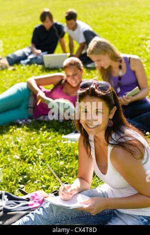 Students studying sitting on grass in park happy teens campus Stock Photo