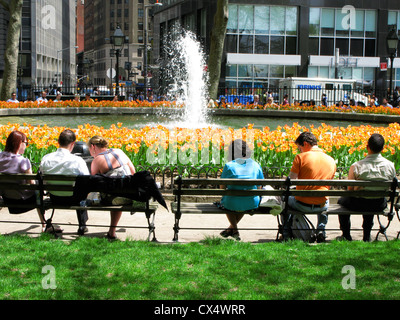 Office workers taking lunch, sitting on benches in front of fountain and orange tulips, sunny day, Bowling Green, off Broadway. Stock Photo