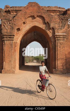 Girl riding bicycle through outer gate, Dhamma-Yangyi Temple (Dhammayangyi), Bagan, Myanmar (Burma) Stock Photo