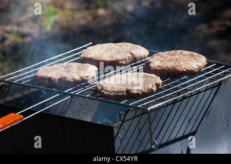 Four raw Hamburgers on Barbeque Grill with smoke Stock Photo