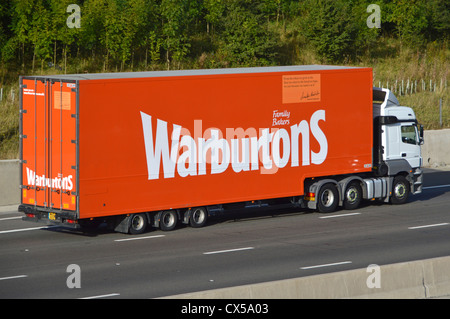 Warburtons family owned bakery business details advertised on side of bread delivery supply chain lorry truck & trailer driving along M25 motorway UK Stock Photo