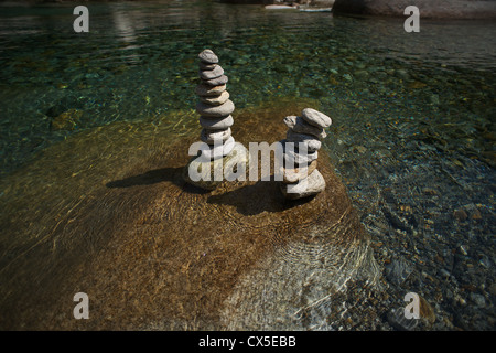 Stacked stones on a rock in the river of Verzasca. Green water flowing around it. Stock Photo
