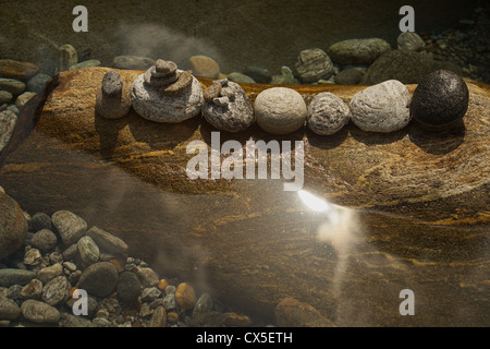 Stones in a row on a mother rock in water with sun shining through the clouds. river Verzasca in Ticino. Stock Photo
