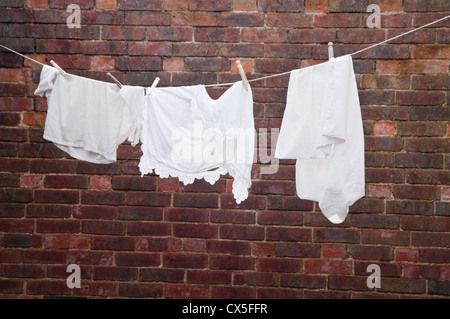 A re-creation of a Victorian washing line within a brick walled yard - with white garments hanging on a rope and dolly pegs. UK. Stock Photo