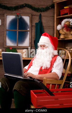Santa Claus Sitting in Rocking Chair in Workshop Using Laptop. Vertical composition. Stock Photo
