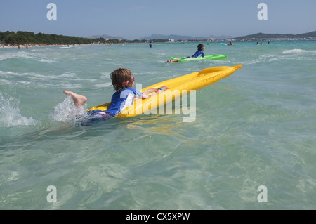 young boys play on beach in the waves on  inflatable lilos Stock Photo