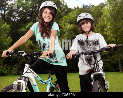 Two happy smiling children in cycling helmets on their bicycles in a park, brother and sister, 10 and 13. Stock Photo