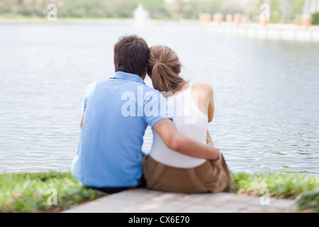 An affectionate couple sitting by a lake, rear view Stock Photo