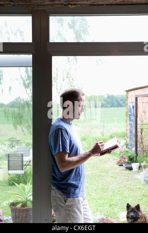 A man leaning against a doorway in his house writing in a journal Stock Photo