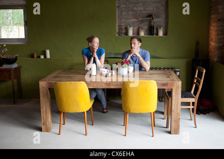 A couple sitting at a dining table looking at each other uncertainly Stock Photo