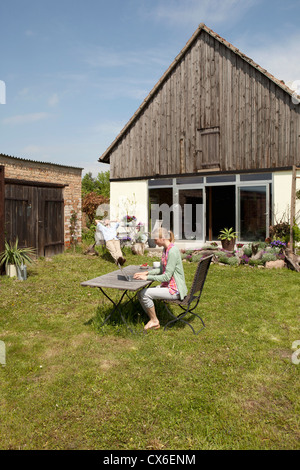 A woman using a laptop and having breakfast in her backyard Stock Photo