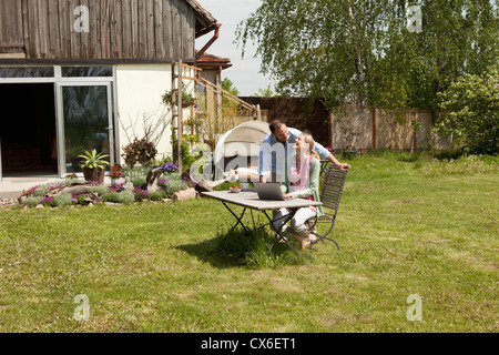 A woman laughing with her boyfriend while using a laptop in her backyard Stock Photo