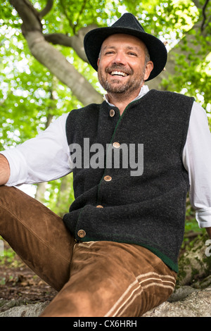 Laughing man in Bavarian costume sitting in a forest on a sunny day Stock Photo