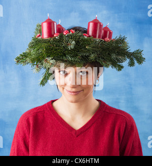 Pretty young woman wearing advent wreath with four candles on her head, xmas studio shot against a blue and white background. Stock Photo