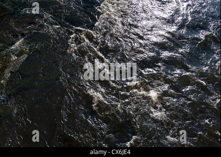 Flowing river water with sparkling sunshine glinting off the fast shallow water.  Ideal background or wallpaper image Stock Photo