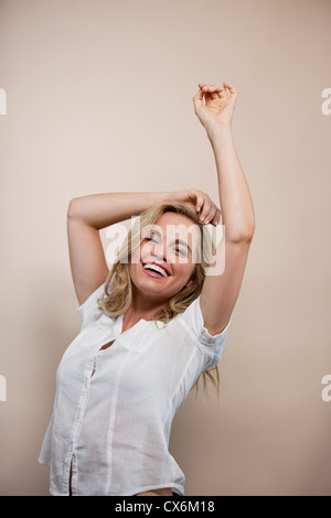 A young blonde woman, arms raised in the air, smiling Stock Photo