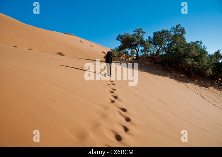 Foot tracks in a Saharan sand dune lead to a man, his face covered by a black scarf. Stock Photo