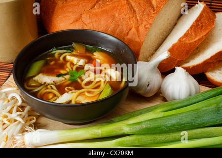 chicken noodle soup a popular and favorite variety worldwide surrounded by ingredients and crusty bread Stock Photo