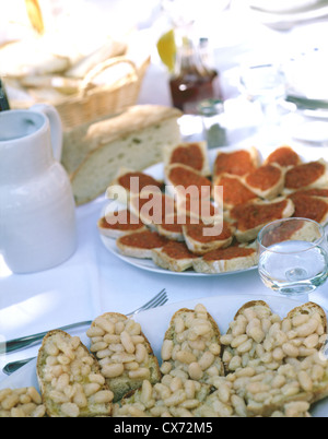 Still Fattoria La Vialla: Table with white cloth, on top plates with bean and tomato crostini Stock Photo