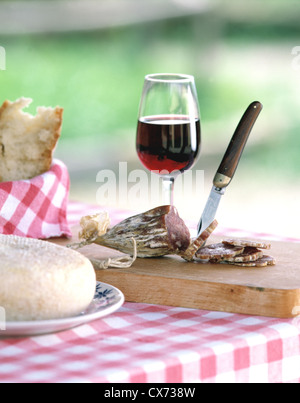 Still Fattoria La Vialla: Table with red - white - checkered cloth, wooden board with sausage, redwine glass Stock Photo