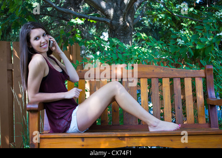 Pretty teen girl talking on phone on a bench outside - copyspace Stock Photo