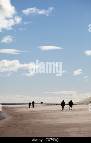 Three couples walking along the sandy beach near Bamburgh Northumberland north east England UK Stock Photo