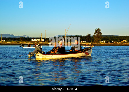 Guide and anglers rowing traditional rowboat to fish for chinook in Tyee Pool at mouth of Campbell River BC Canada at sunrise Stock Photo