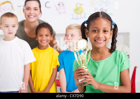 african american preschool girl holding a trophy in front of classmates Stock Photo