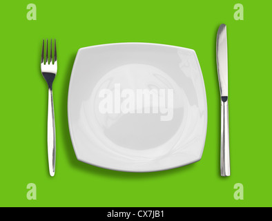Knife, square white plate and fork on green background Stock Photo