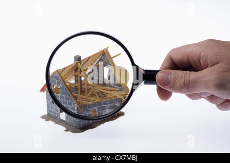 A human hand holding a magnifying glass up to a partially constructed miniature house model Stock Photo