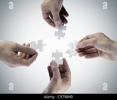 Four hands holding jigsaw puzzle pieces, directly above Stock Photo