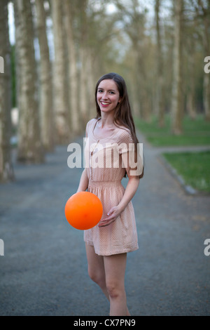 A young woman holding an orange ball, standing in a park Stock Photo