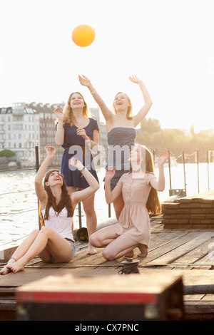 Four female friends tossing a ball around on a jetty next to Spree River, Berlin, Germany Stock Photo