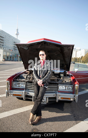 A cool rockabilly guy holding tools leaning against the front of his vintage car, hood up Stock Photo