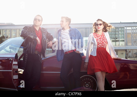 Three rockabilly friends leaning against a vintage car Stock Photo