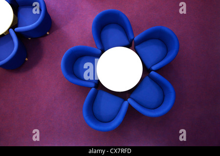 Blue chairs surrounding white table looking like a flower, chairs as petals on bright colour purple carpet taken from above Stock Photo