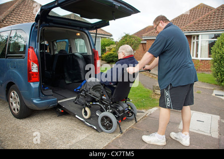 Male Carer son pushing a disabled elderly man in a wheelchair onto a built in ramp in a specially adapted car for getting about Stock Photo