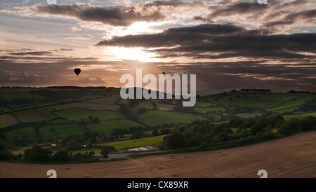Aerial view of three hot air balloons silhouetted against setting Sun over patchwork quilt countryside near Bristol Stock Photo