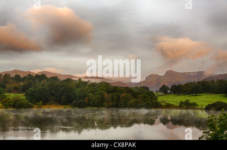 Sun rising and illuminating Langdale Pikes with Loughrigg Tarn in foreground Stock Photo